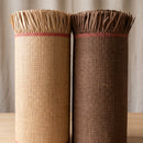 Side-by-side rolls of authentic woven lauhala island mats in natural beige and dark chocolate with frayed fringe edges