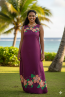 A woman wearing a long purple maxi dress made from Hibiscus Double Border Polyester Fabric, featuring a tropical peach and orange hibiscus floral pattern along the hem and neckline, with a beach and palm tree background.