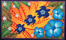 A flat-lay view of the Hibiscus, Plumeria Assortment Sarong (Style 5) featuring a vibrant Polynesian-inspired design. The pattern includes large, detailed blue hibiscus flowers and smaller white plumeria blossoms set against a bright orange and yellow background. The design is layered with traditional tribal motifs, including three stylized dark blue sea turtles (honu) swimming across the center, and various geometric tattoo-inspired patterns in the background.
