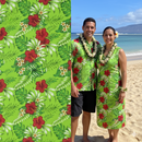 Couple wearing custom island apparel in Hibiscus Plumeria Tropical Leaves All Over Design Cotton Fabric with a tropical beach and ocean background.