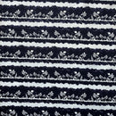repeating fabric pattern featuring white silhouettes of tropical island scenes on a dark navy blue background. The scenes include palm trees, small thatched-roof huts (tiki huts), and sailboats, arranged in horizontal bands separated by textured, wave-like white lines.