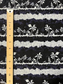 A close-up view of the Lagoon Nights Rayon fabric featuring a repeating tropical island pattern in white silhouettes on a dark navy blue background. A wooden ruler is placed vertically along the left side of the fabric to show the scale of the design, with the repeating horizontal bands of palm trees, tiki huts, and sailboats measuring approximately 3 to 4 inches each in height.