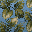 A top-down view of fabric featuring a tropical pattern of large, detailed green Monstera and palm leaves on a solid light blue background.